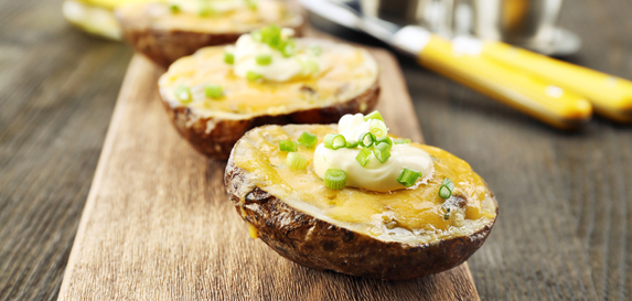 Three potato halves topped with cheese, chives and sour cream sit on a thick wood serving tray.